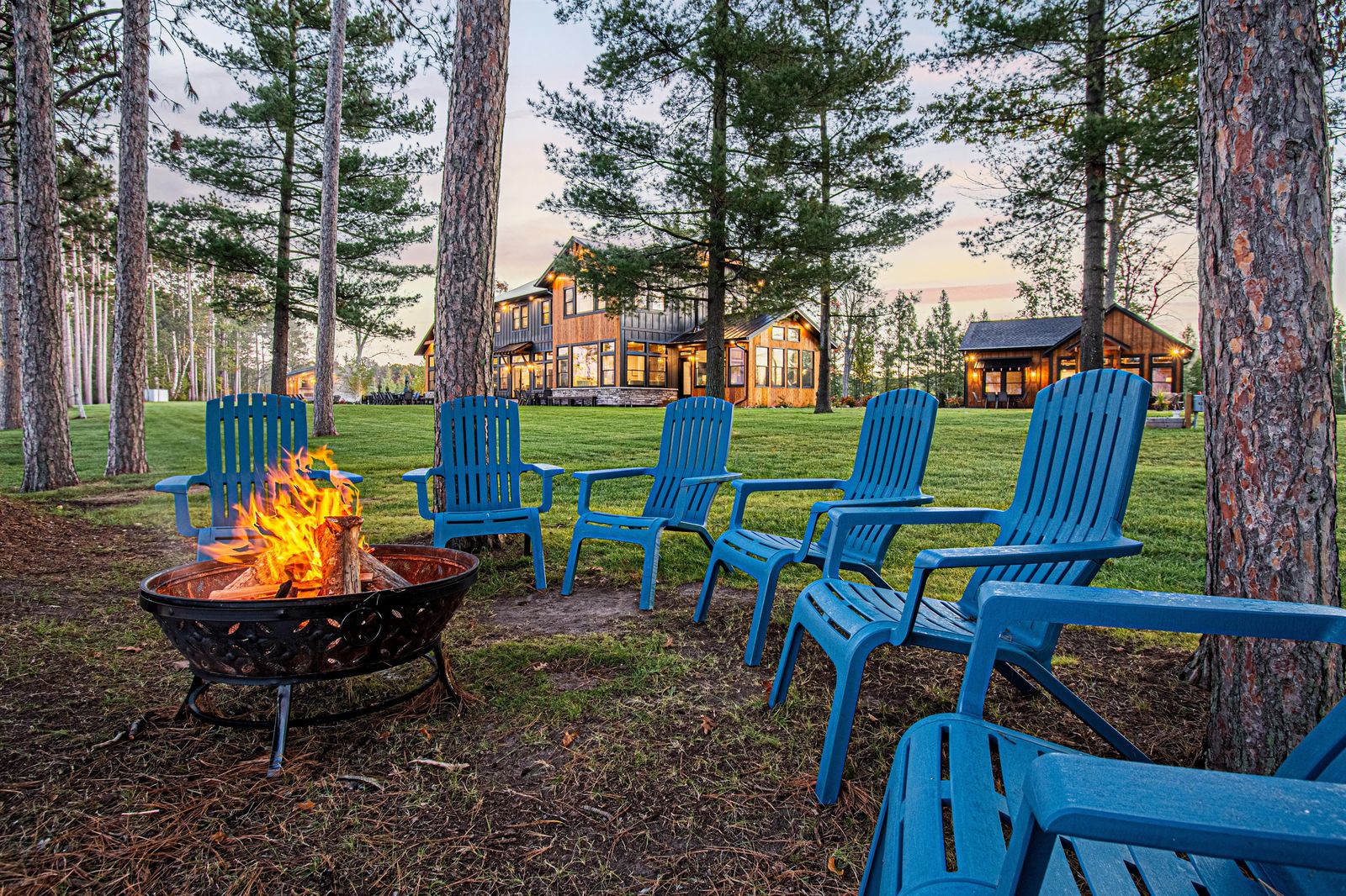 Adirondack chairs circled around a lakeside fire pit in the evening
